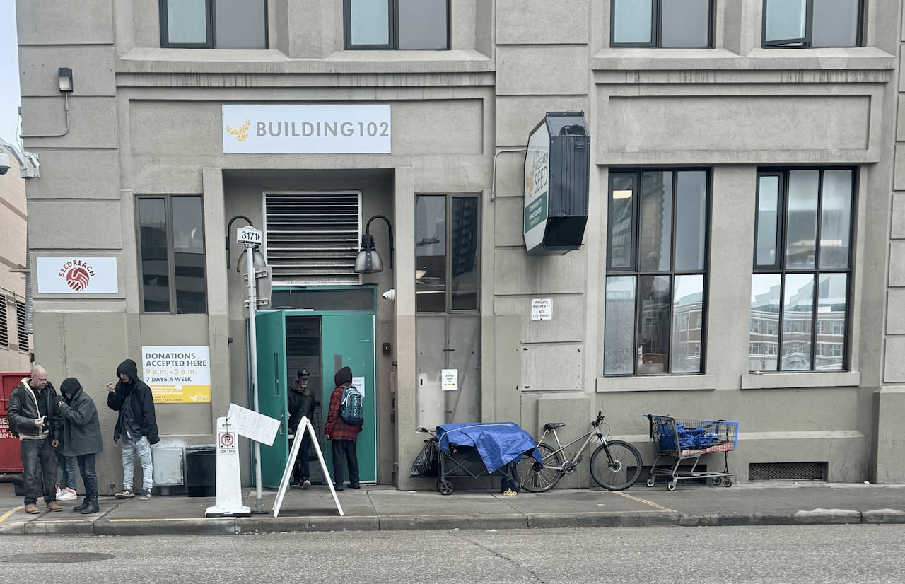 People standing outside a city building with bikes and shopping carts, smoking.