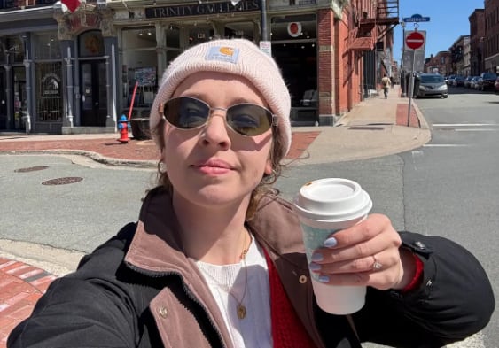 A woman in a coat and toque holds up a coffee