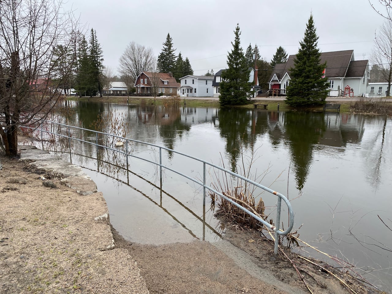 A river is seen with higher than normal water levels, which are submerging a half of a fence.