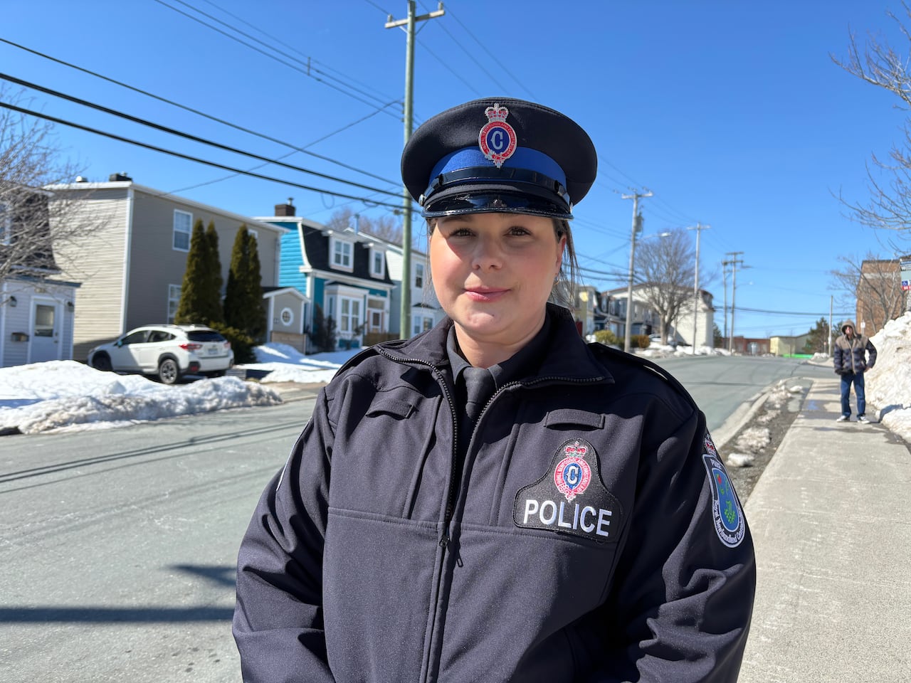 A woman in uniform standing on a sidewalk. A row of houses is in the background. 