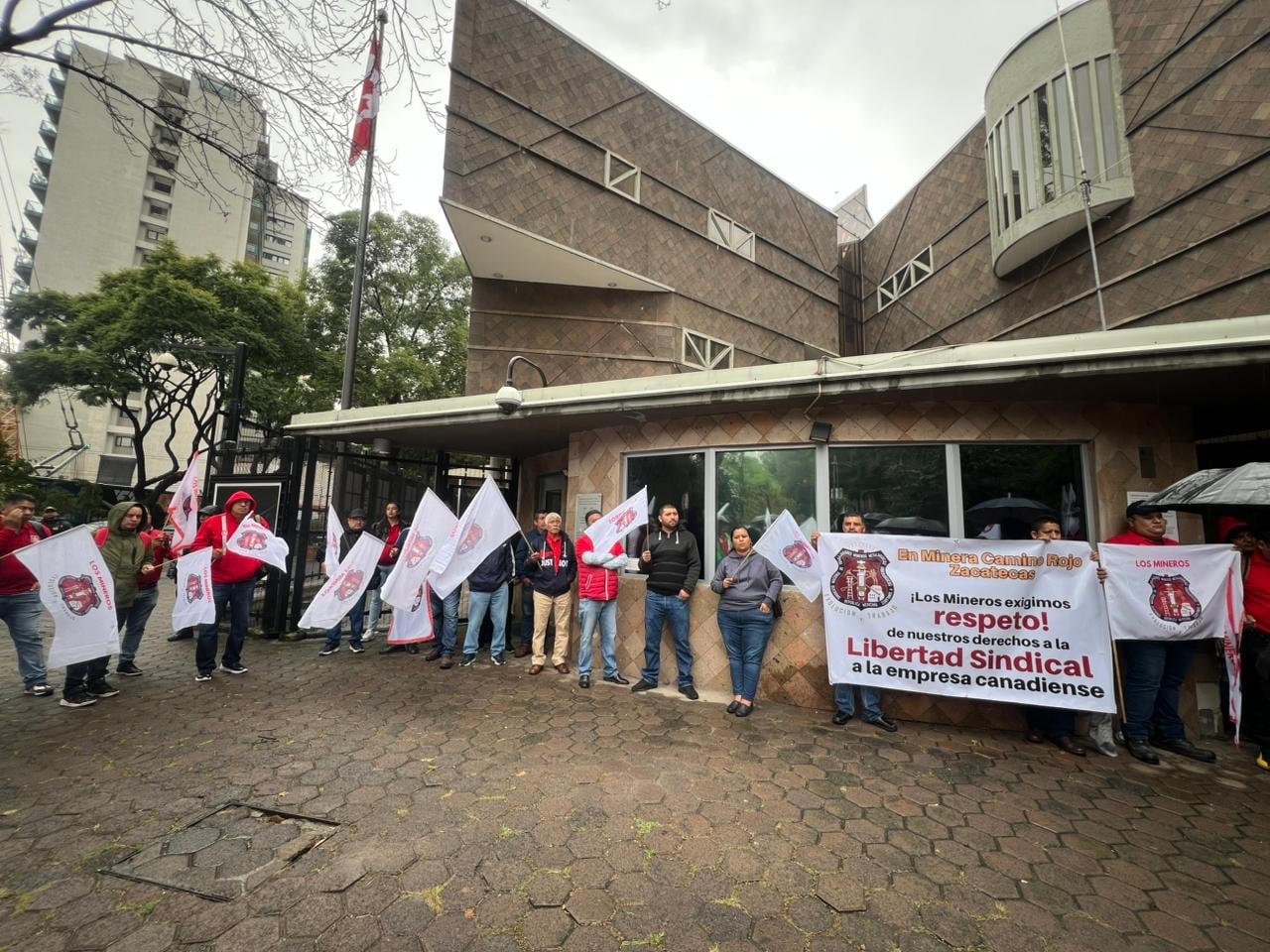 A group stands in front of a buiding with a large banner and white flags with union logos.