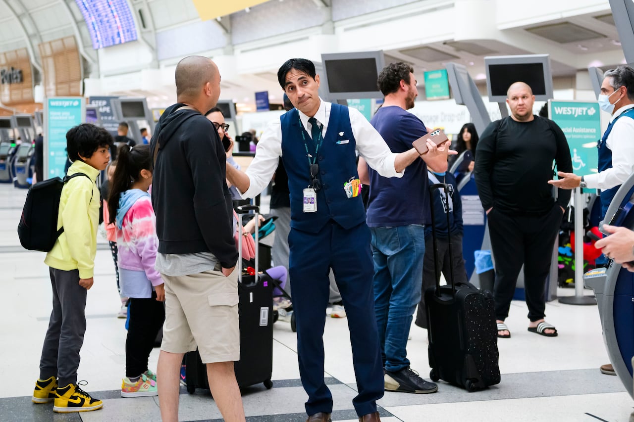 A man in a uniform holds his hands up in a shrug while speaking to another man.