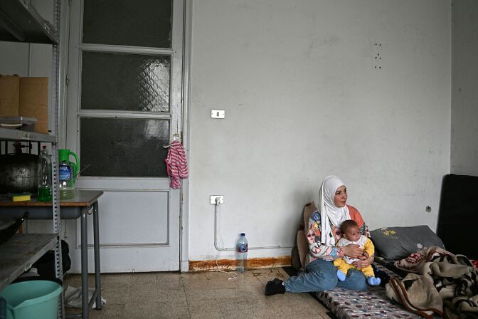 A woman sits on the floor while holding a toddler in her lap.