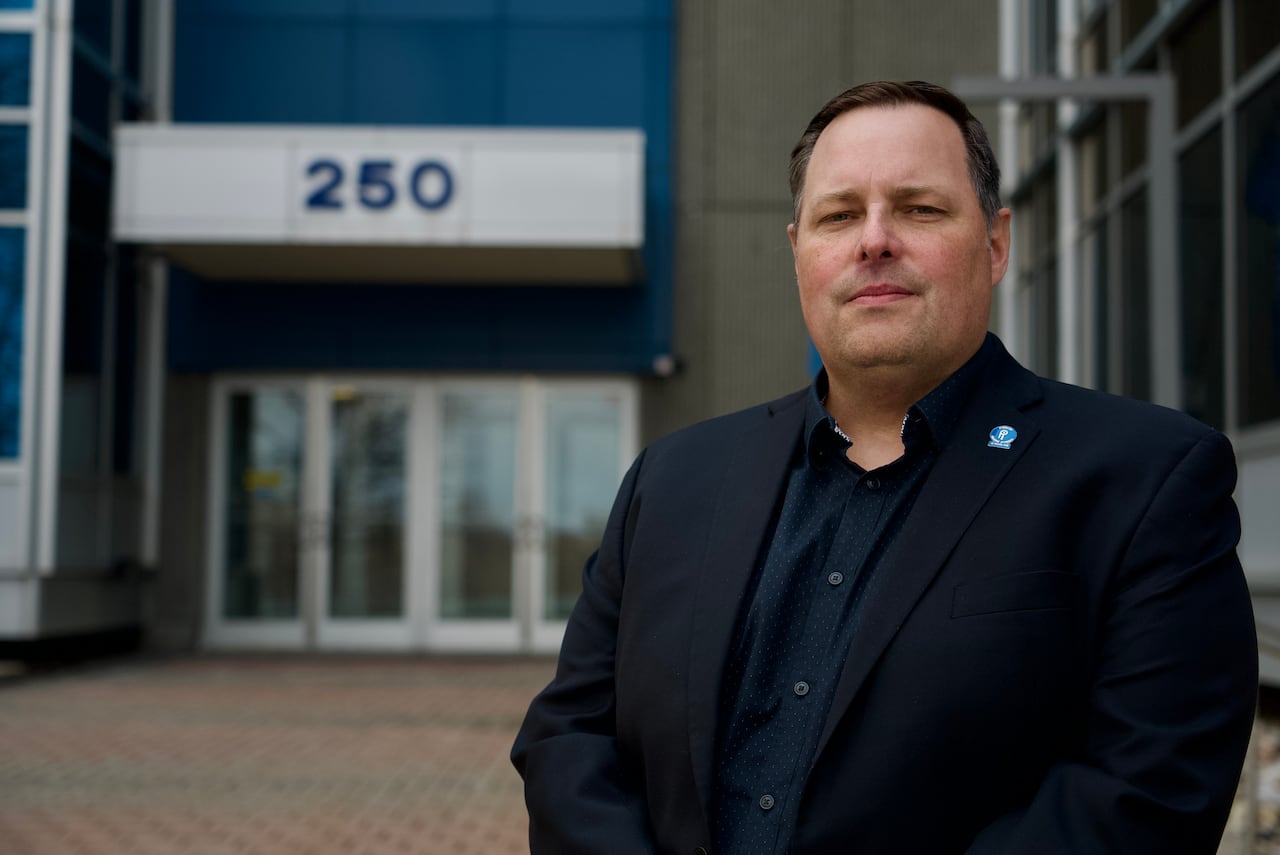 A man in a blue suit stands in front of a government building.