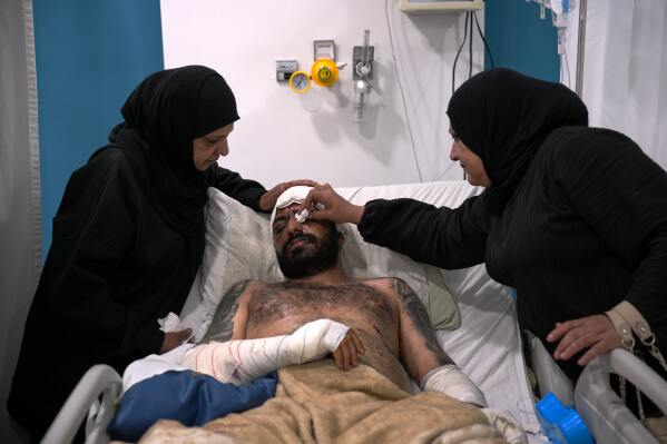 Mahmoud Sahmarani, 33, rests in a hospital bed as he is comforted by his mother and aunt after being injured in an Israeli airstrike, at Al-Najda Al-Shaabiya Hospital, in Nabatiyeh, southern Lebanon, Friday, April 17, 2026, following a ceasefire between Israel and Hezbollah. (AP Photo/Hassan Ammar)