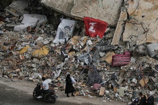 Residents pass the rubble of destroyed buildings, where a Hezbollah flag and an image of its late leader Hassan Nasrallah are placed, in Dahiyeh, Beirut's southern suburbs, Lebanon, Friday, April 17, 2026, following a ceasefire between Israel and Hezbollah. (AP Photo/Bilal Hussein)