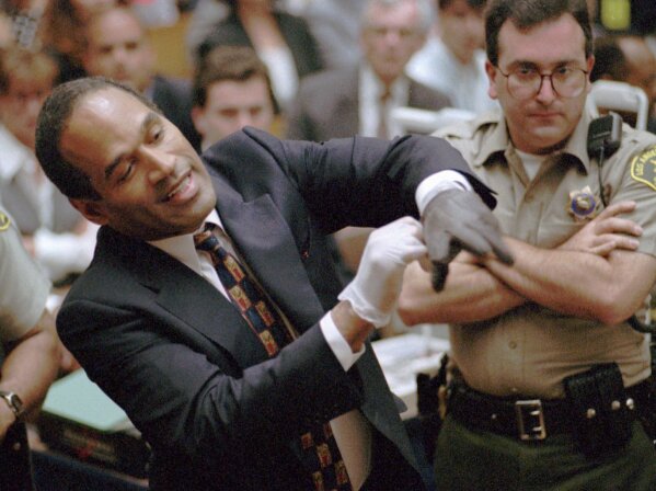 In this June 15, 1995 file photo, O.J. Simpson, left, grimaces as he tries on one of the leather gloves prosecutors say he wore the night his ex-wife Nicole Brown Simpson and Ron Goldman were murdered in a Los Angeles courtroom. (AP Photo/Sam Mircovich, Pool, file)