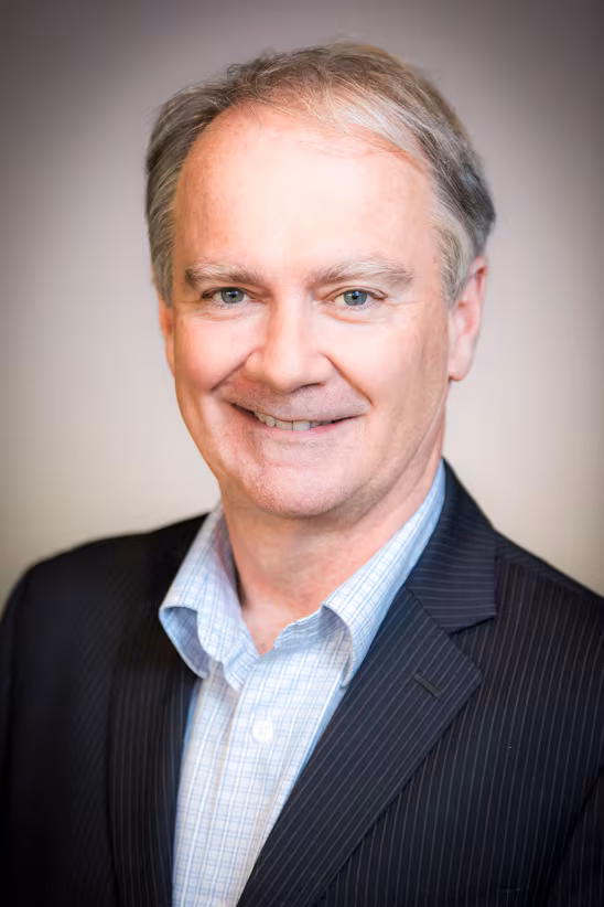 Man in dark-coloured suit in front light-coloured backdrop
