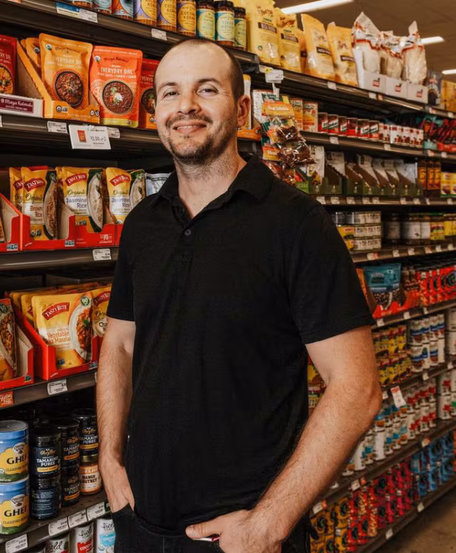Man wearing black polo stands with hands in pockets in a grocery isle