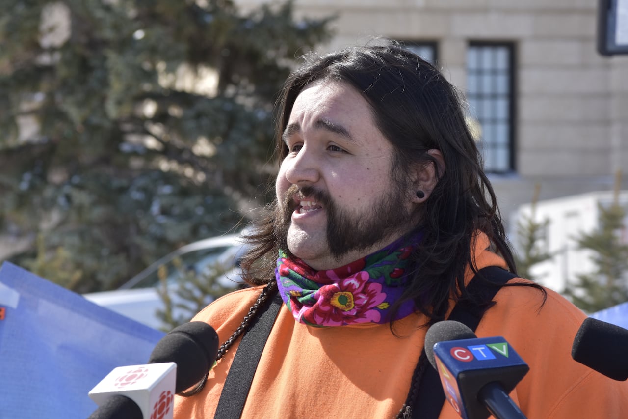 A man in an orange shirt speaks to media.