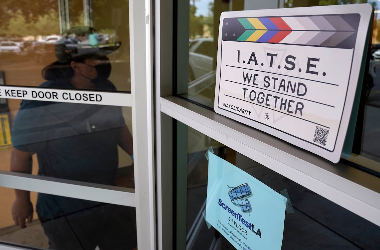 A man enters the union offices of The International Alliance of Theatrical Stage Employees, which features a clapboard with the words 'IATSE We stand together'.