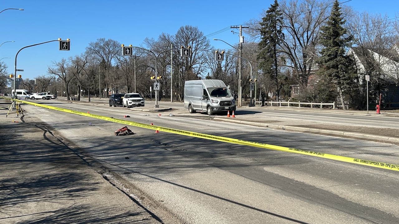 A suburban main street is blocked off with yellow police tape and several orange pylons