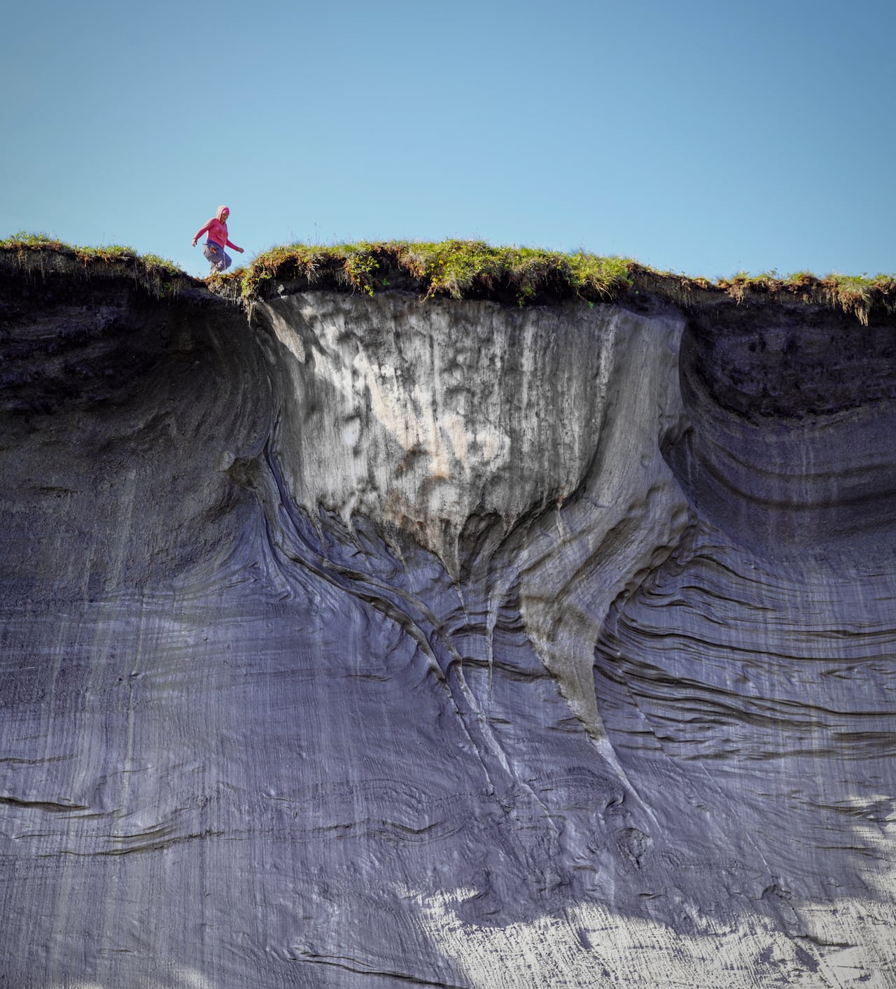 A woman walks along the top of a tall cliff edge