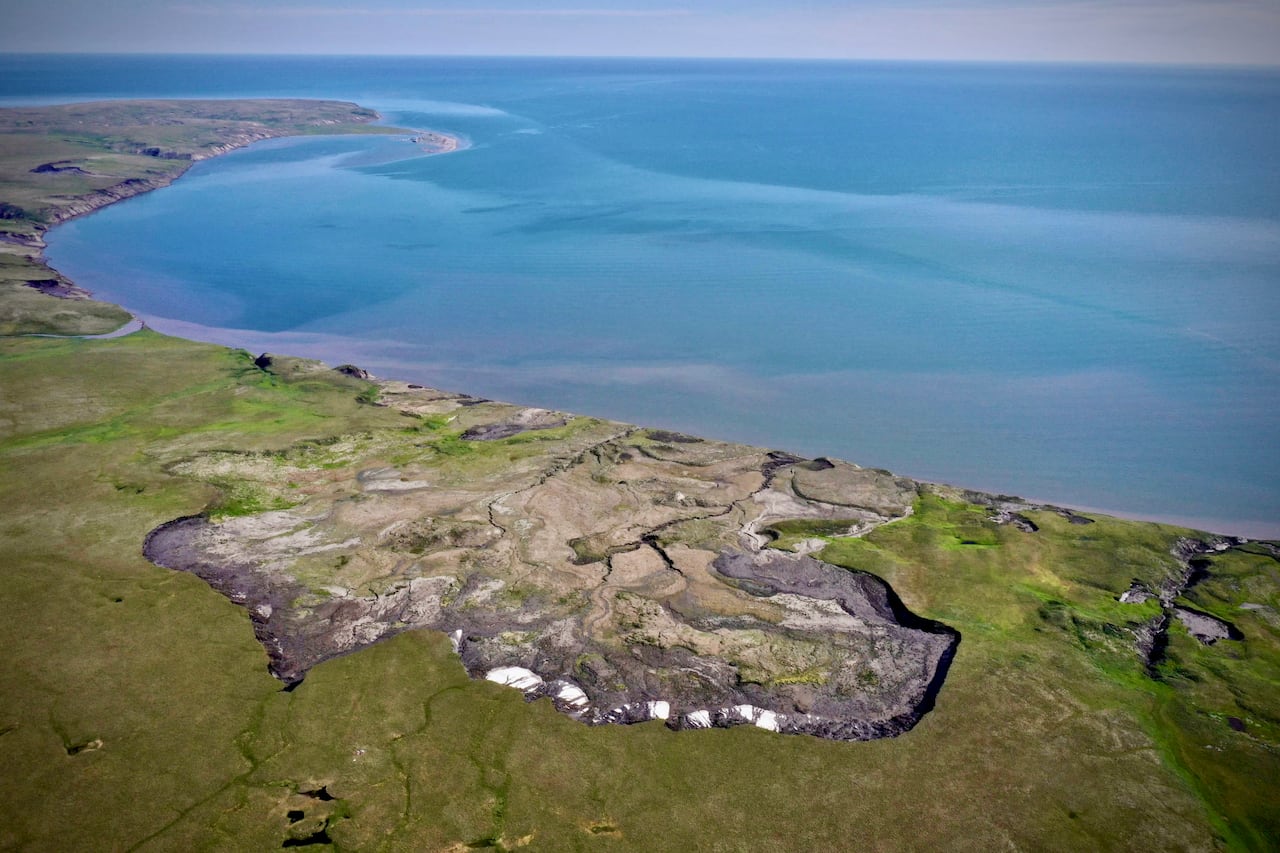 An aerial shot of a large depression in a green landscape next to a body of water.