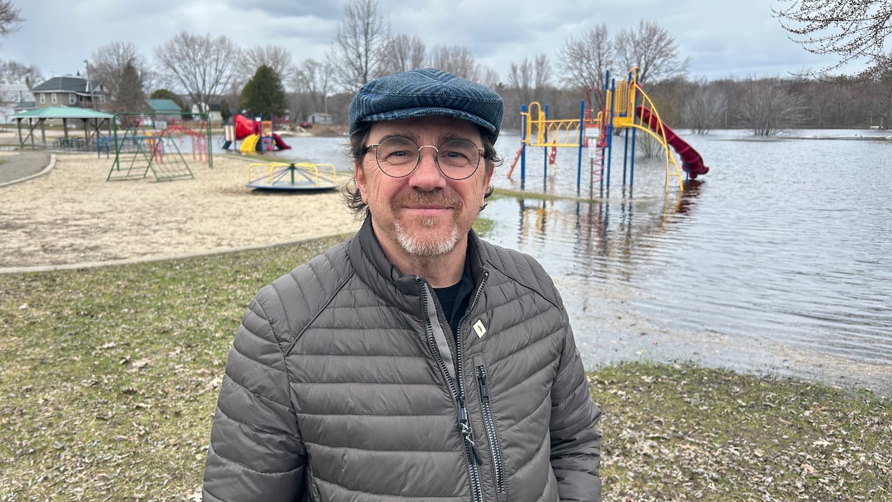 a man with a cap and glasses standing in front of a flooded playground