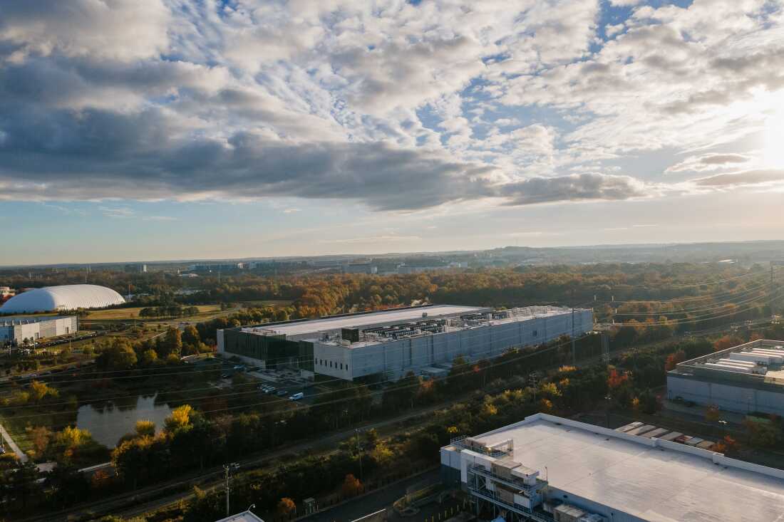This photo taken from high above shows a Meta data center in Ashburn, Virginia, in 2025. It is a large, long light-colored building with few windows, and it's nestled among trees and a few other buildings with a similar shape.