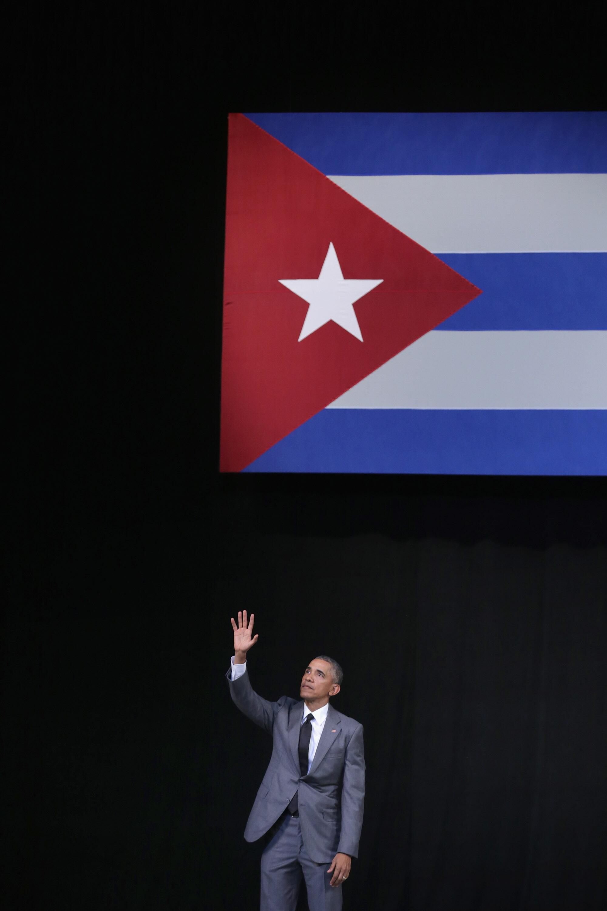 President Obama waves to the crowd in front of a flag of Cuba