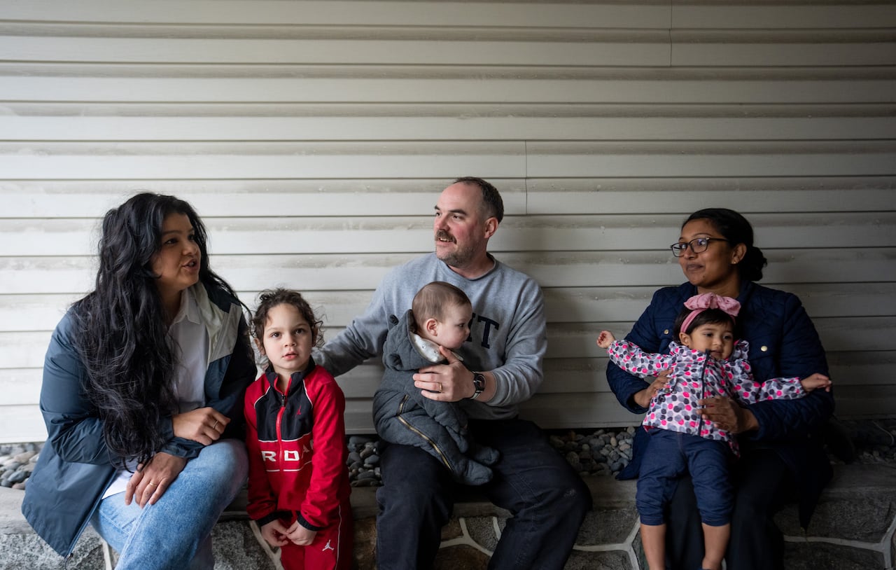 A group of two women, a man and three young children sit on a curb.