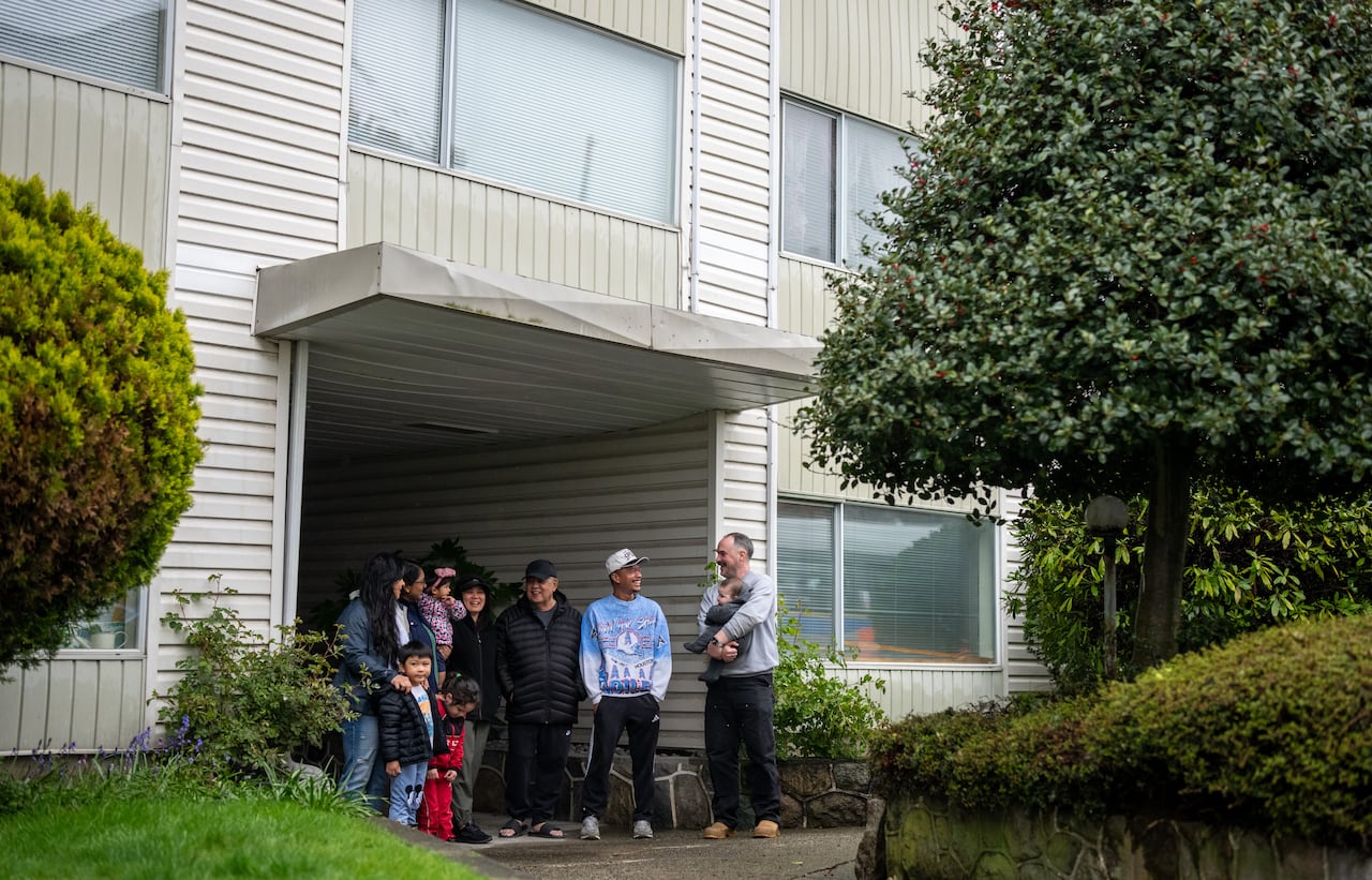 A group of about 10 people stand outside the entrance to an older apartment building.