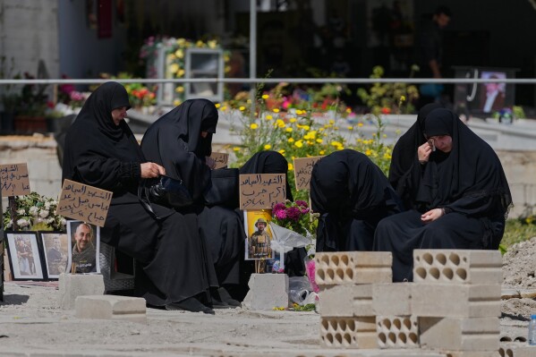 Relatives of a Hezbollah fighter mourn on his grave at a cemetery where civilians and Hezbollah fighters killed in Israeli airstrikes are temporarily buried in the southern port city of Sidon, Lebanon, Tuesday, April 14, 2026. (AP Photo/Mohammed Zaatari)