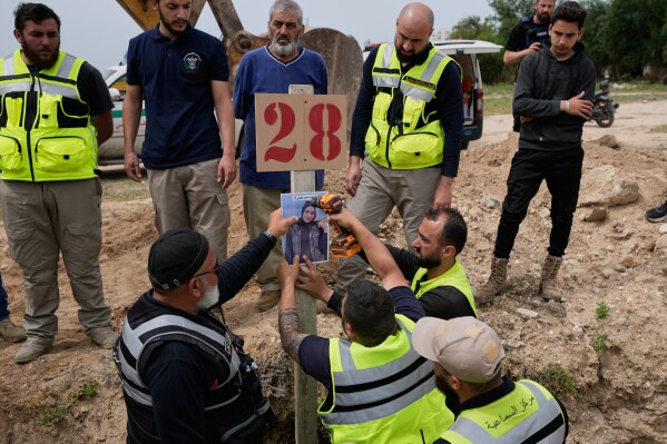 Paramedics attach a portrait over the grave of Ghadir Baalbaki, 19, who was killed on Tuesday in an Israeli airstrike, at a temporary mass grave in the southern port city of Tyre, Lebanon, Wednesday, April 15, 2026. (AP Photo/Hussein Malla)