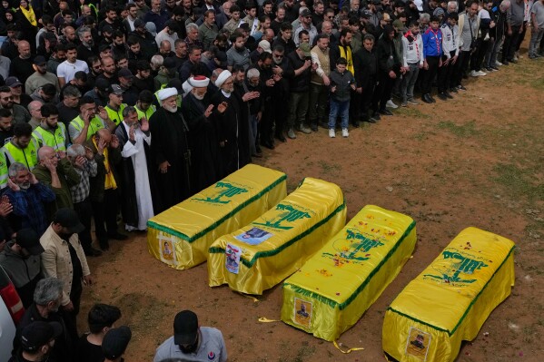 Mourners pray on the coffins of Hezbollah fighters and civilians who were killed in the war between Hezbollah and Israel during a mass funeral in Bazouriyeh village, south Lebanon, Monday, April 20, 2026. (AP Photo/Mohammed Zaatari)