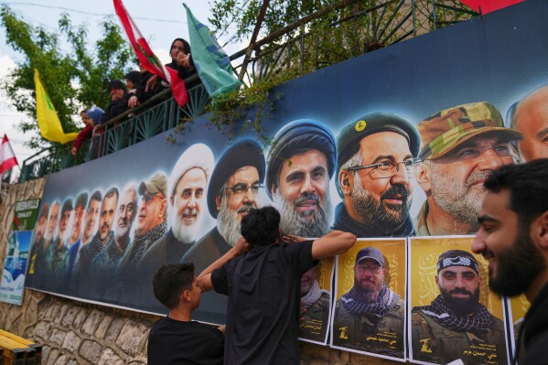 Hezbollah supporters hang portraits of Hezbollah fighters killed in Israeli airstrikes during their funeral procession in the southern village of Kfar Sir, Lebanon, Tuesday, April 21, 2026. (AP Photo/Hassan Ammar)