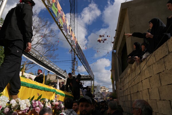 A woman, right, throws flowers over the coffins of Hezbollah fighters, who were killed before the ceasefire in the war between Hezbollah and Israel, during a mass funeral procession in the southern village of Kfar Sir, Lebanon, Tuesday, April 21, 2026. (AP Photo/Hassan Ammar)