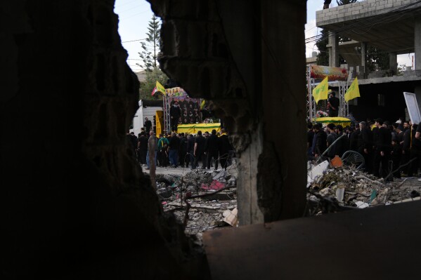 A semi transporting coffins that contain the remains of Hezbollah fighters who were killed before the ceasefire in the war between Hezbollah and Israel, drives past the rubble of a destroyed building, as part of a mass funeral procession in the southern village of Kfar Sir, Lebanon, Tuesday, April 21, 2026. (AP Photo/Hassan Ammar)
