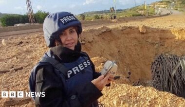Photo of Al Akhbar journalist Amal Khalil, wearing a press jacket and helmet, reporting near a destroyed bridge in Qasmiyeh.