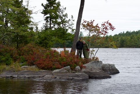 A male and a female standing on a tip of an island across the water