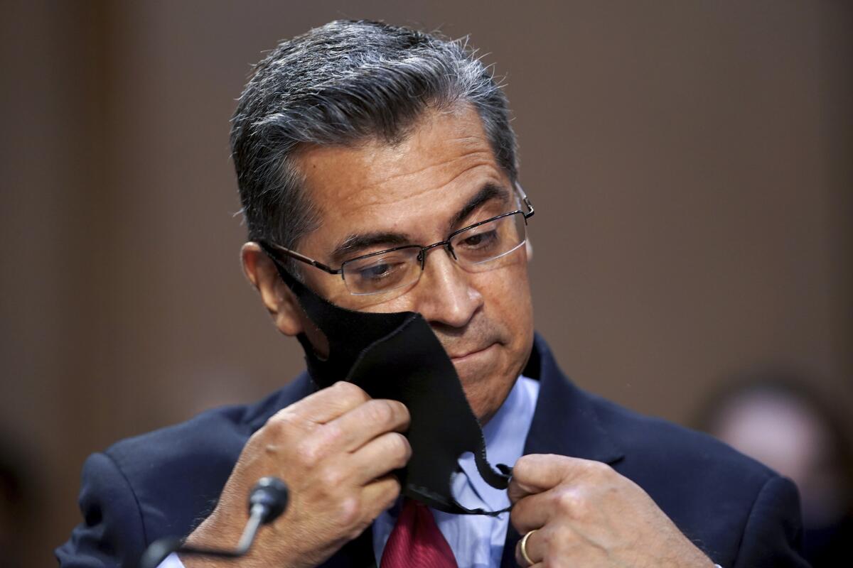 Xavier Becerra removes a face mask during a hearing