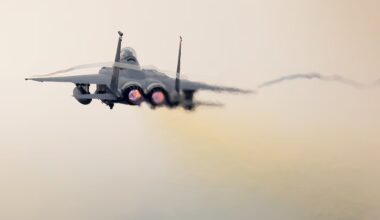 A twin-engine military fighter jet flies through a hazy sky.