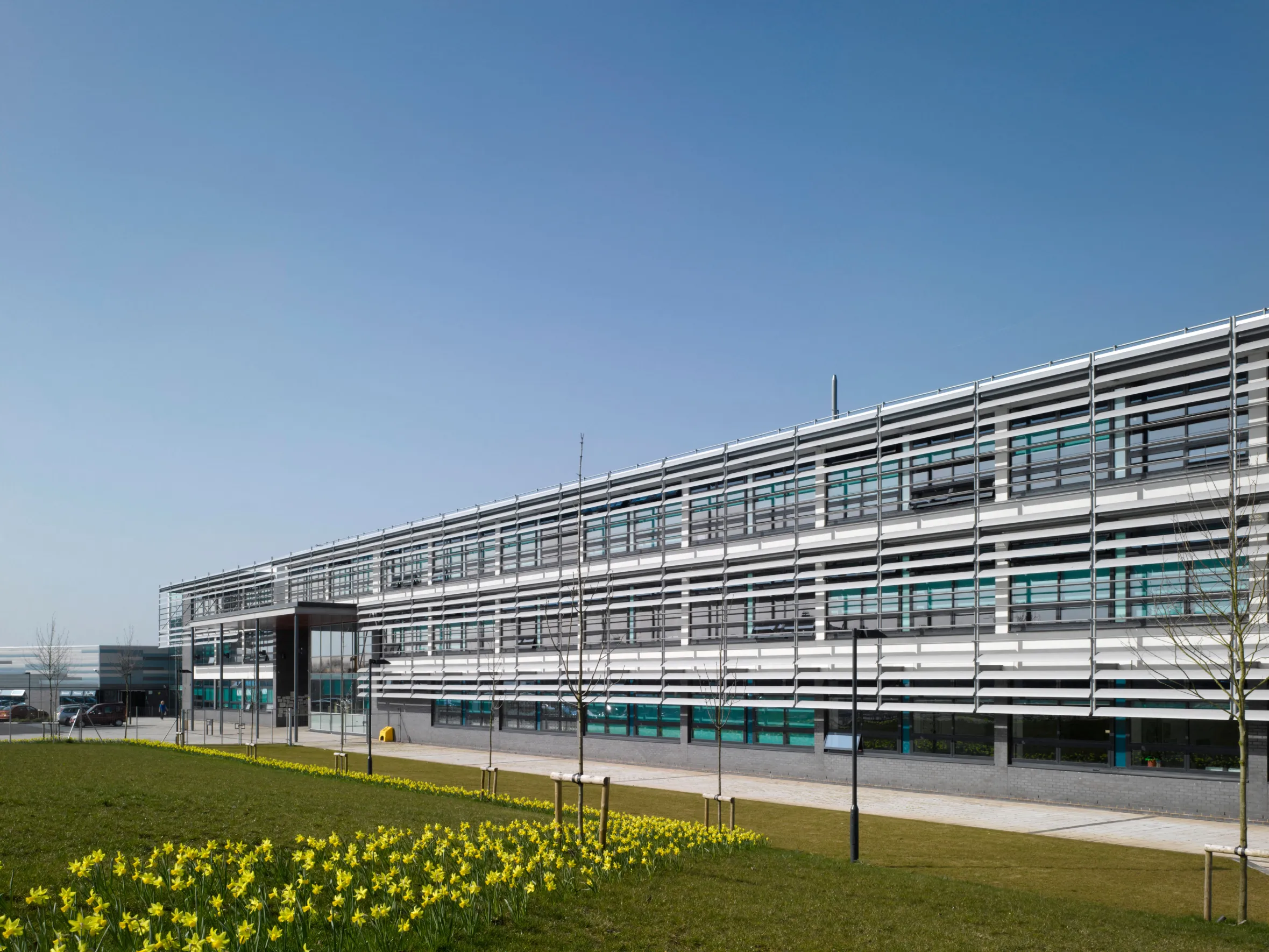Bristol Brunel Academy, a modern secondary school building with a facade featuring horizontal white panels and windows, set against a clear blue sky.