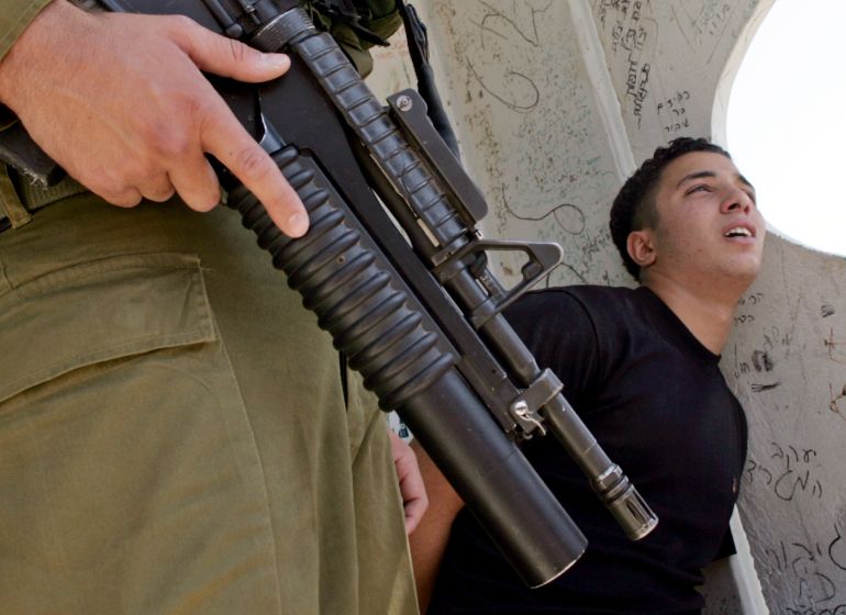 An Israeli soldier guards Palestinian youth Hasan Khalifeh, 15, after he is arrested near the West Bank city of Nablus on August 29, 2005 [Abed Omar Qusini/Reuters]