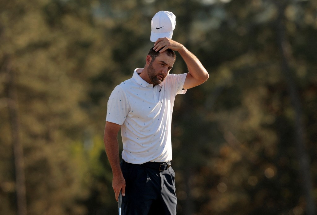 Scottie Scheffler removes his white cap, holding it just above his head, and appears frustrated on the 18th hole at the Masters.