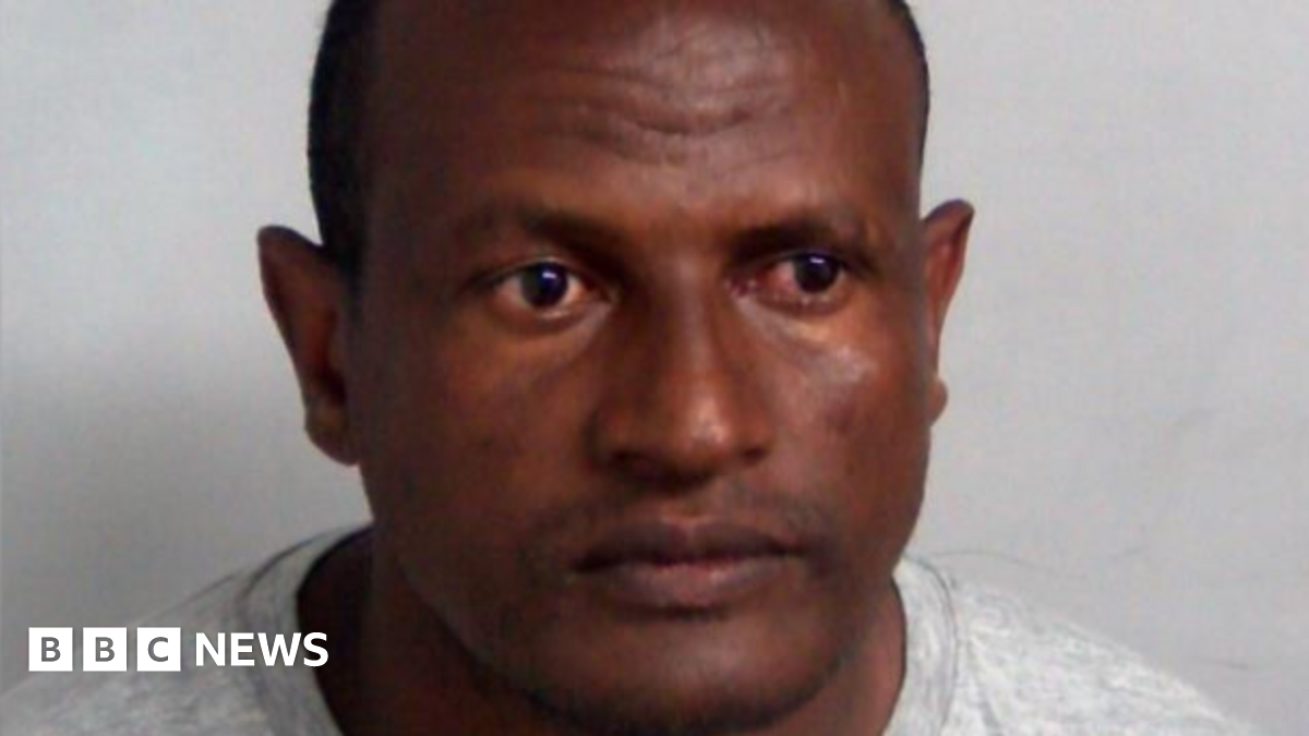 A custody photo of Hadush Kebatu, who is wearing a grey sweater and has cropped black hair.