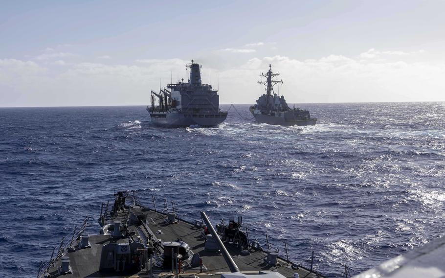 View from the bow of a U.S. Navy destroyer looking toward a fleet replenishment oiler and another destroyer conducting an underway replenishment at sea.