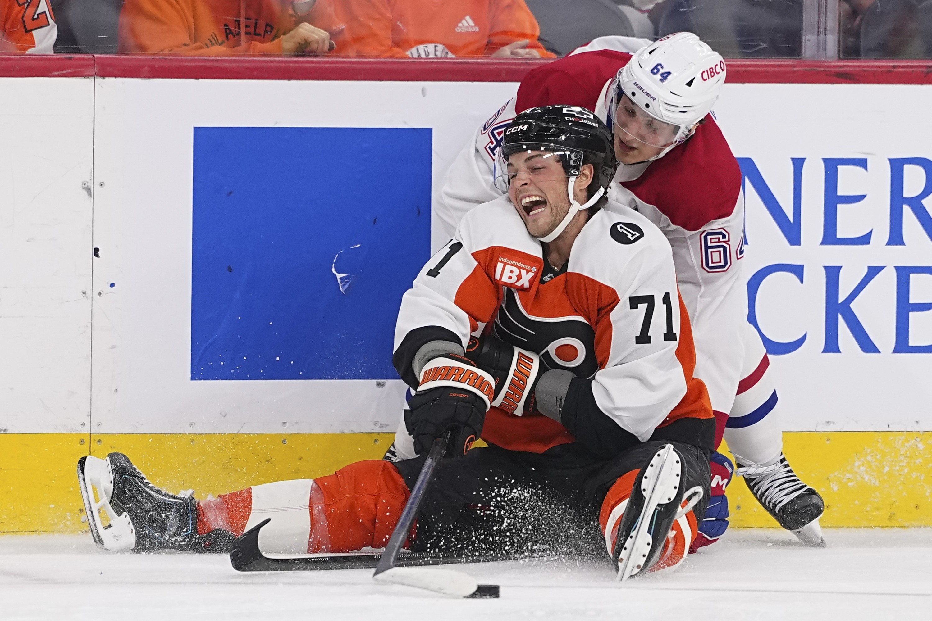 Tyson Foerste of the Philadelphia Flyers tries to play the puck while sitting on the ice, with Canadiens' David Reinbacher behind him.