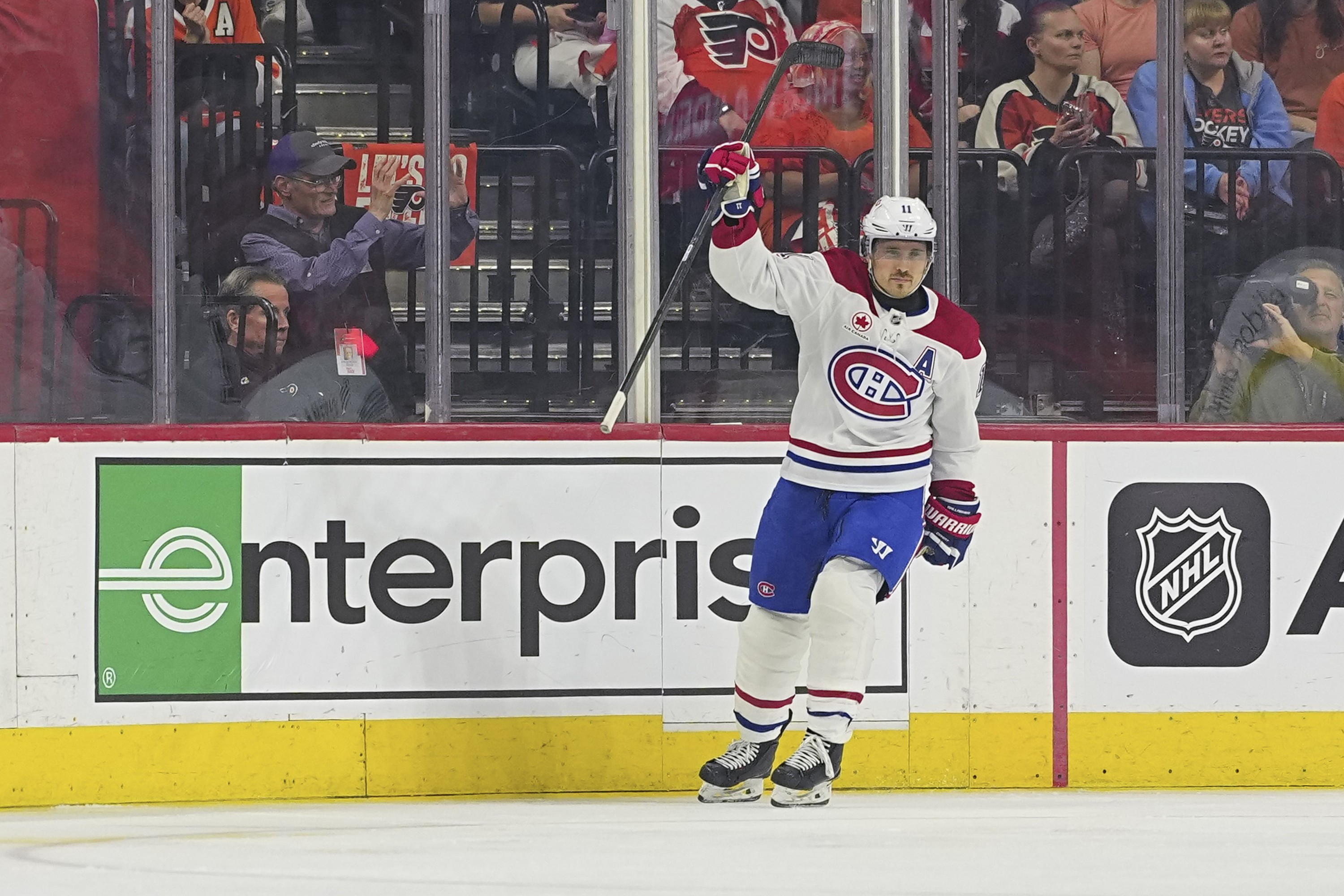 Brendan Gallagher holds his stick up as he skates near the boards while Flyers fans in the stands look unimpressed.