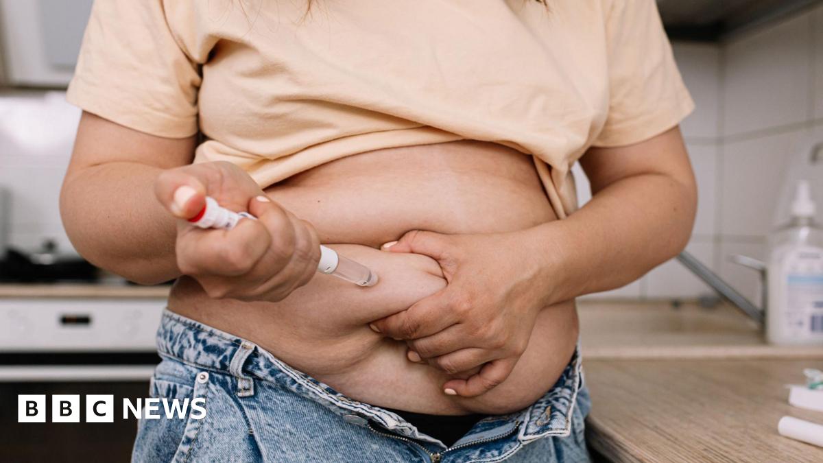 A woman uses a pre-filled injection pen to administer a dose. She is lifting her t-shirt to be able to inject.