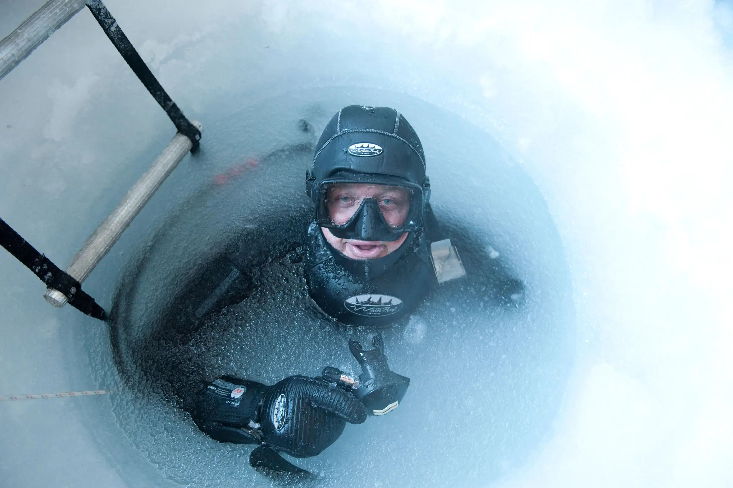 Cameraman Doug Allan at the frozen water surface of a drilled ice hole.