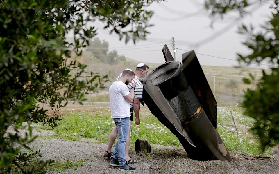 An Israeli man looks at the tail section of a ballistic missile launched from Iran, in the Jewish settlement of Shadmot Mehola in the northern Jordan Valley on April 03, 2026 in Shadmot Mehola, Israel
