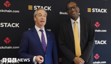 Reform UK leader Nigel Farage (L) stands with former Chancellor Kwasi Kwarteng (R) as they promote cryptocurrency. Farage wears a dark blue suit, a white shirt and a blue tie with red blossoms. Kwarteng wears a black suit,  a white shirt and a butter yellow tie.