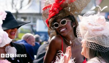 Three you women stand talking and smiling outside. They are wearing elaborate, formal headwear.