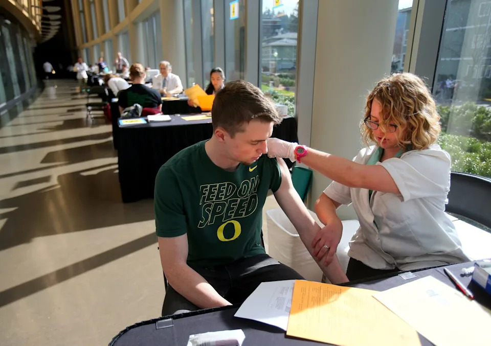 In this Monday, March 2, 2015 photo, pharmacist Jenna Wright administers the Meningitis B vaccine to University of Oregon freshman Drew Russert during a mass vaccination clinic at Matthew Knight Arena in Eugene, Ore. after an outbreak of meningococcemia, resulting in the death of a student. On Wednesday, June 24, 2015, a federal panel gave a weak endorsement to two new expensive meningitis shots, declining to recommend the vaccines for all teens and leaving the decision to parents and doctors. Students already get another meningitis vaccine that protects against more common strains.