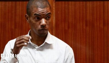 A man wearing a white shirt standing in front of wood panelling