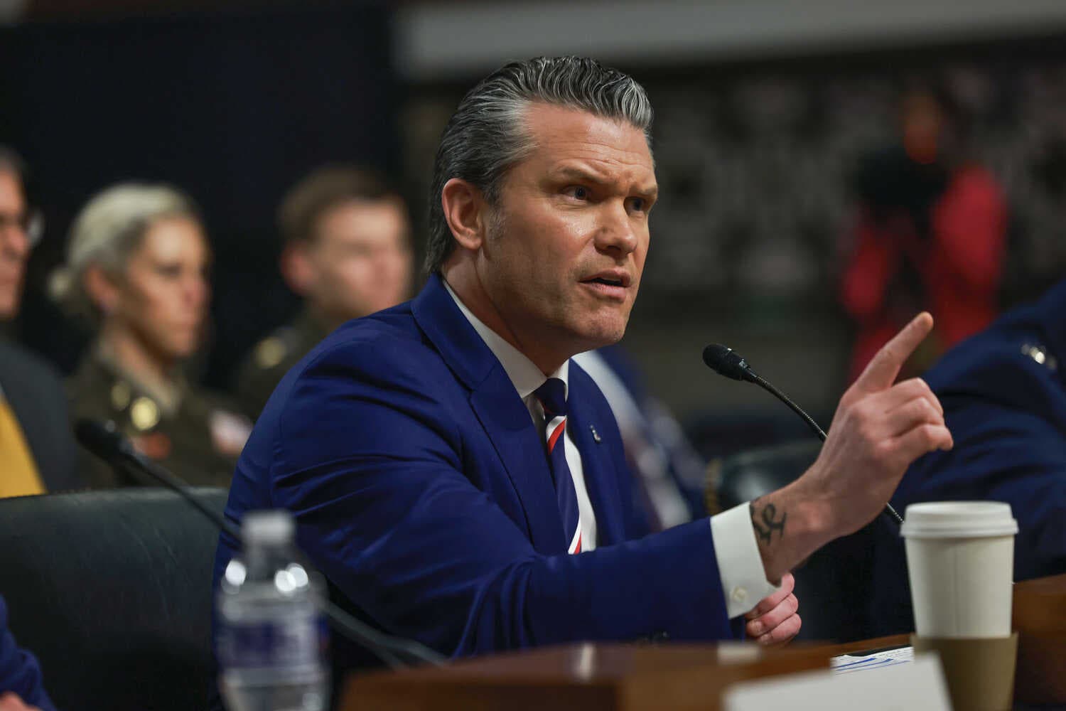 Defense Secretary Pete Hegseth speaking into a microphone with his finger raised.
