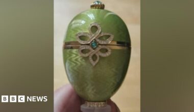 Close-up of a green Fabergé egg ornament featuring a gold band around the centre and a decorative diamond‑patterned design with a small blue‑green gemstone.