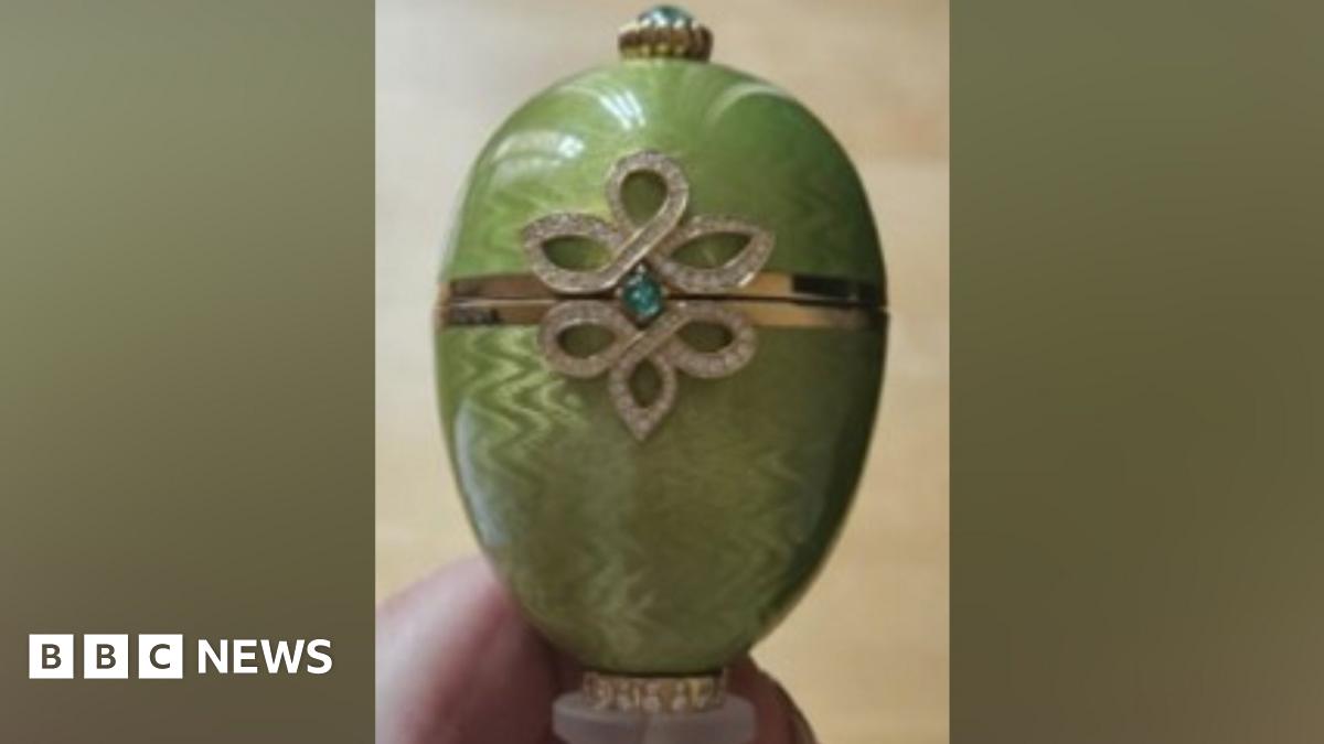 Close-up of a green Fabergé egg ornament featuring a gold band around the centre and a decorative diamond‑patterned design with a small blue‑green gemstone.